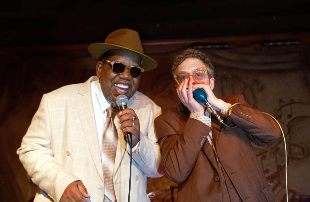 Joe and Oscar shades singing and playing harmonica on stage.