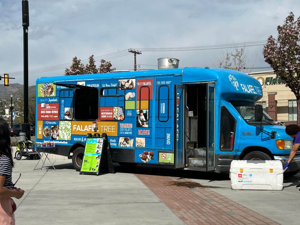 A bright blue Falafel Tree food truck parked on a city street, with a menu board in front and people nearby.